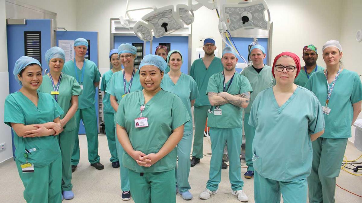 Group of staff in scrubs standing in medical Theatre