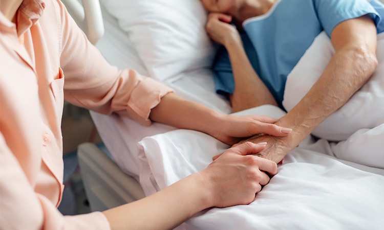 Person holding patients hand, sat next to their bedside in hospital